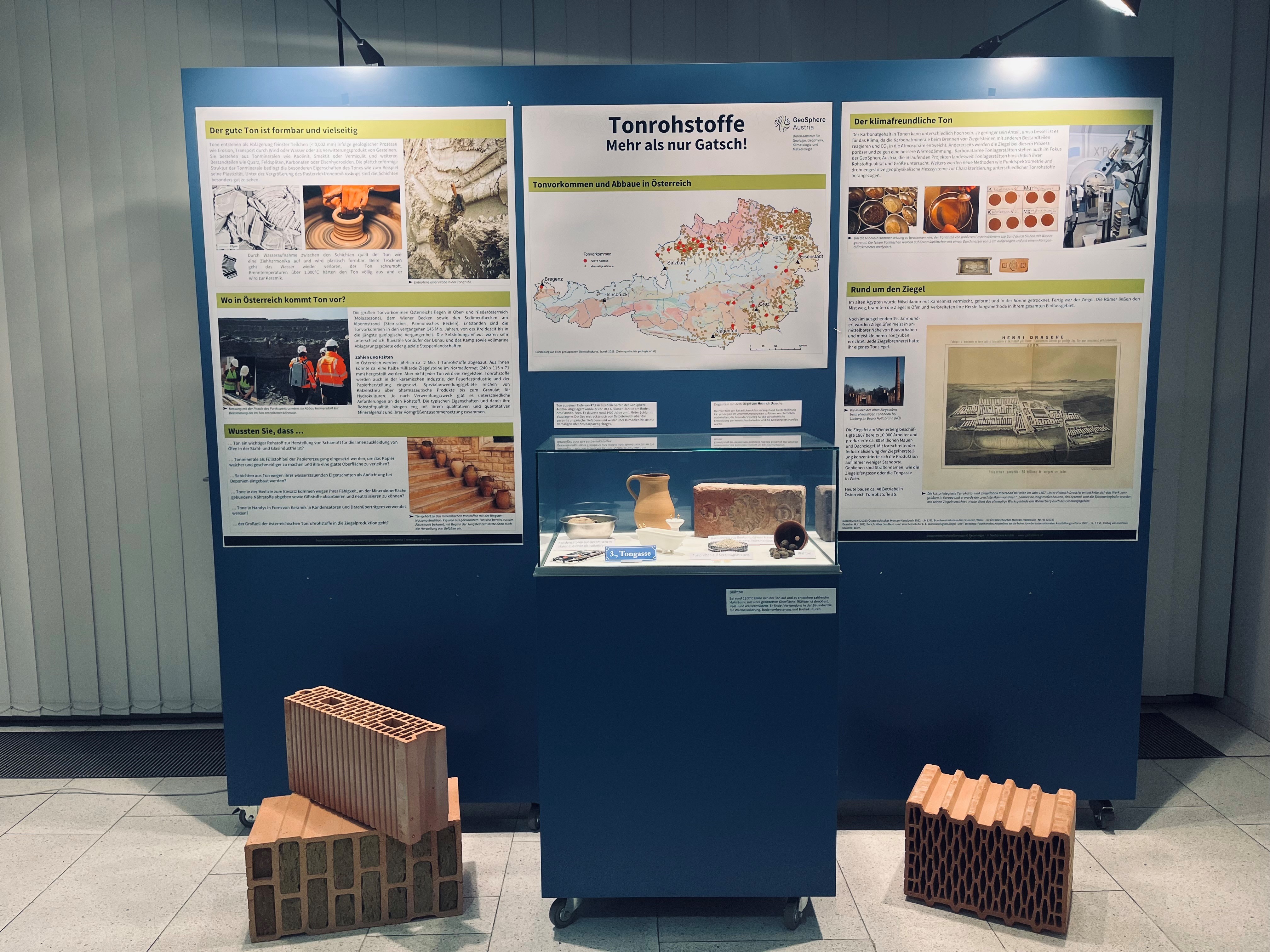 Display with 3 posters, a showcase with clay objects and 3 bricks on the floor.