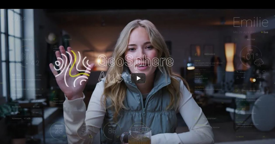 A young blonde woman sits in a room. The palm of her right hand faces the viewer and contains the GeoSphere Austria logo