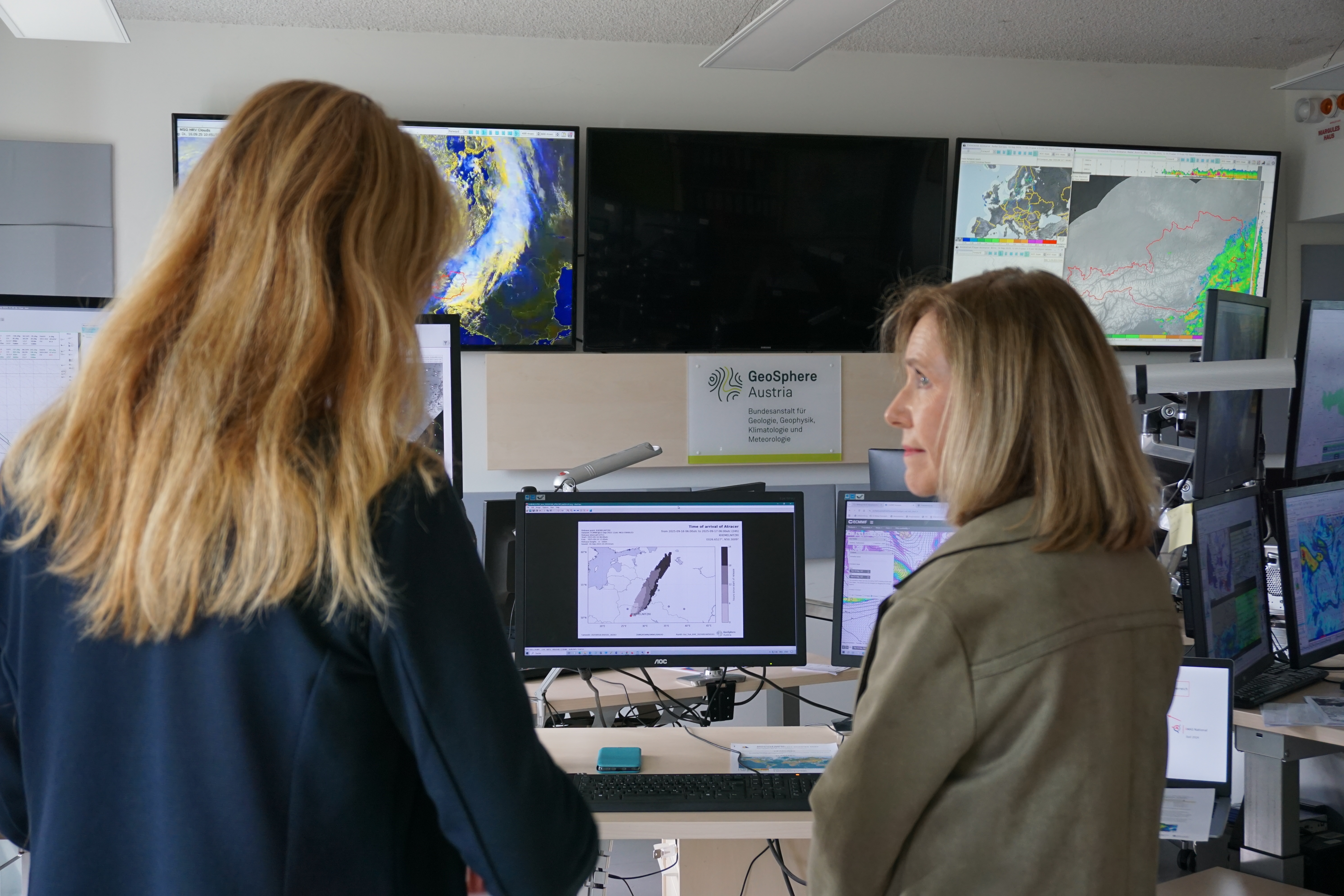 Two women in front of a wall of screens